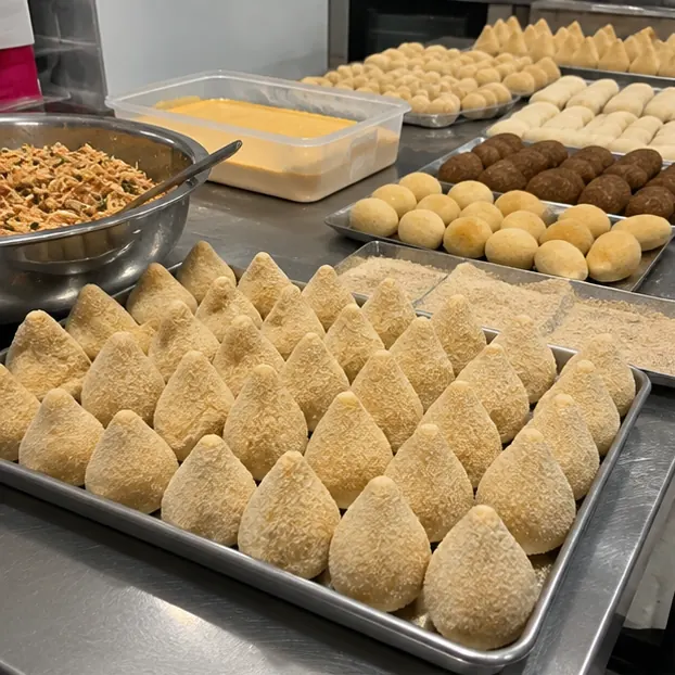 Bancada de produção com bandejas de coxinha empanada e os recheios prontos